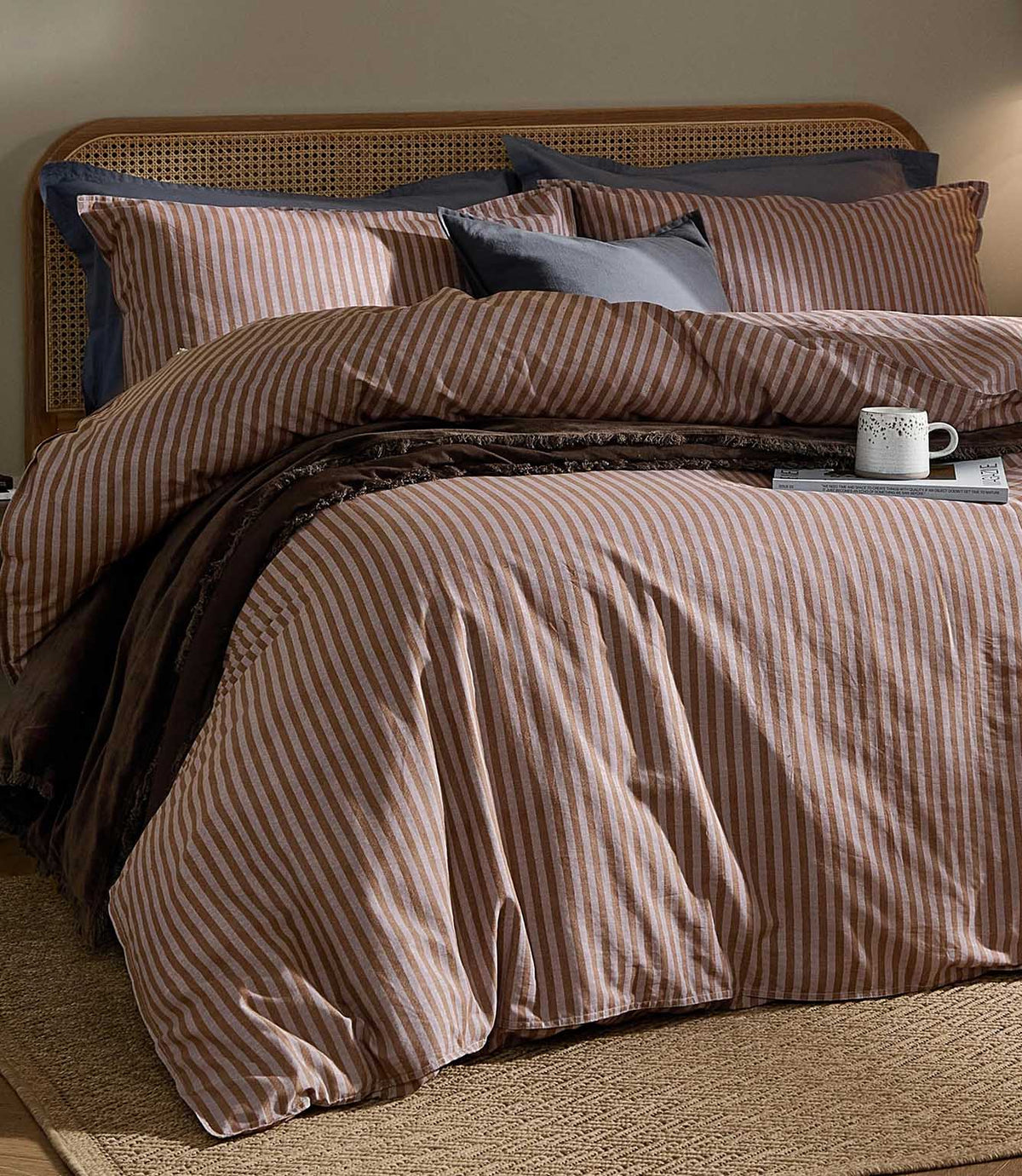 Marlow Stripe Cocoa/Vintage Blue duvet cover and coordinating striped pillowcases styled with vintage blue cushions, a dark brown throw and natural cane headboard.