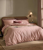 Marlow Stripe duvet cover set in soft blush pink and rose stripes, styled on a bed with coordinating pillows, a textured throw and natural cane headboard.