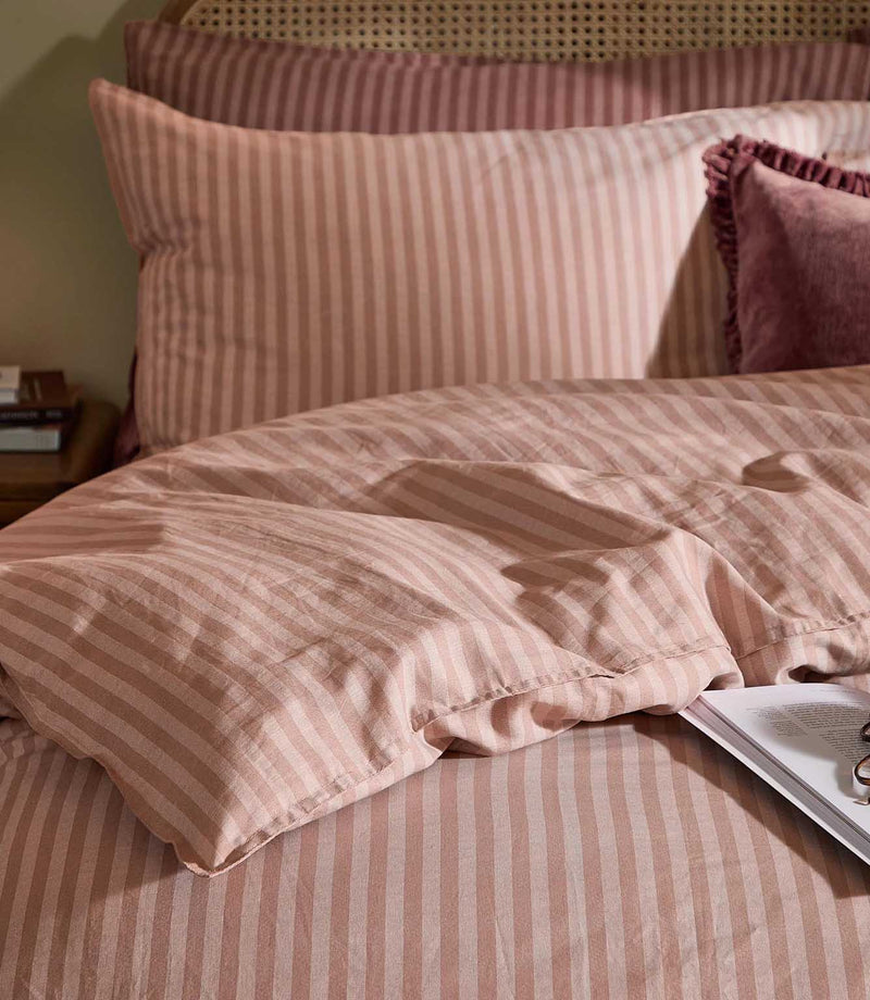 Close-up of Marlow Stripe bedding showing soft blush pink and rose vertical stripes, coordinating pillowcases and the gently crumpled fabric texture.