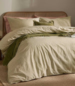 Marlow Stripe olive green and cream duvet cover set styled with matching striped pillowcases, green velvet accents and a natural cane headboard.