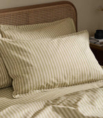 Close-up of Marlow Stripe pillowcases in olive green and cream, showing the classic vertical stripe and gently crumpled fabric finish.