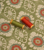 Olive green decorative fabric with coral floral motifs, styled with coordinating sewing threads to highlight colour matching and texture.