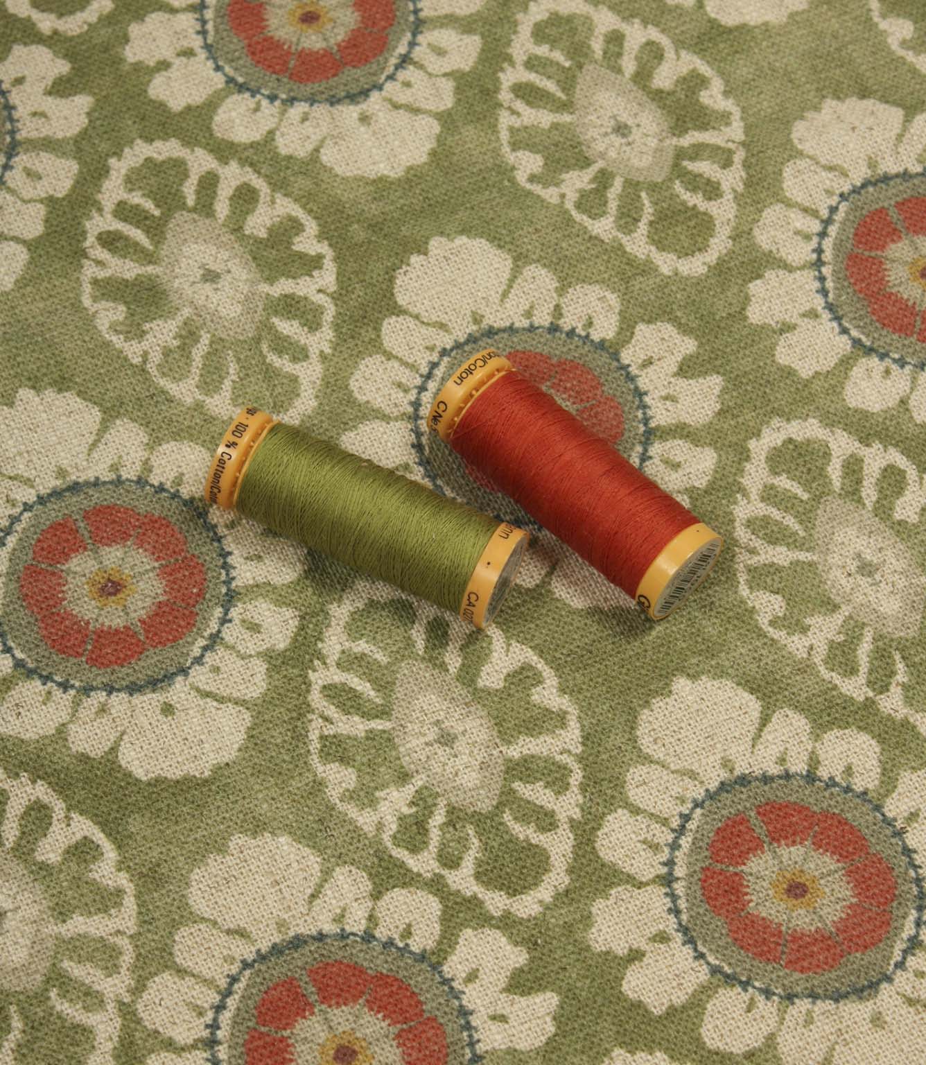 Olive green decorative fabric with coral floral motifs, styled with coordinating sewing threads to highlight colour matching and texture.