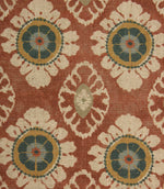Close-up of terracotta red decorative fabric with stylised floral medallions and intricate cream patterning on a textured weave.