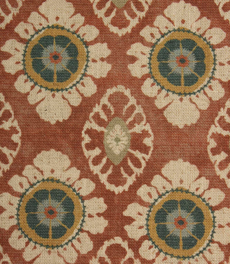Close-up of terracotta red decorative fabric with stylised floral medallions and intricate cream patterning on a textured weave.