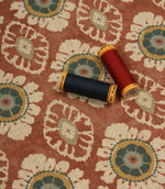 Terracotta floral print fabric styled with coordinating sewing threads to showcase rich warm tones and woven texture.