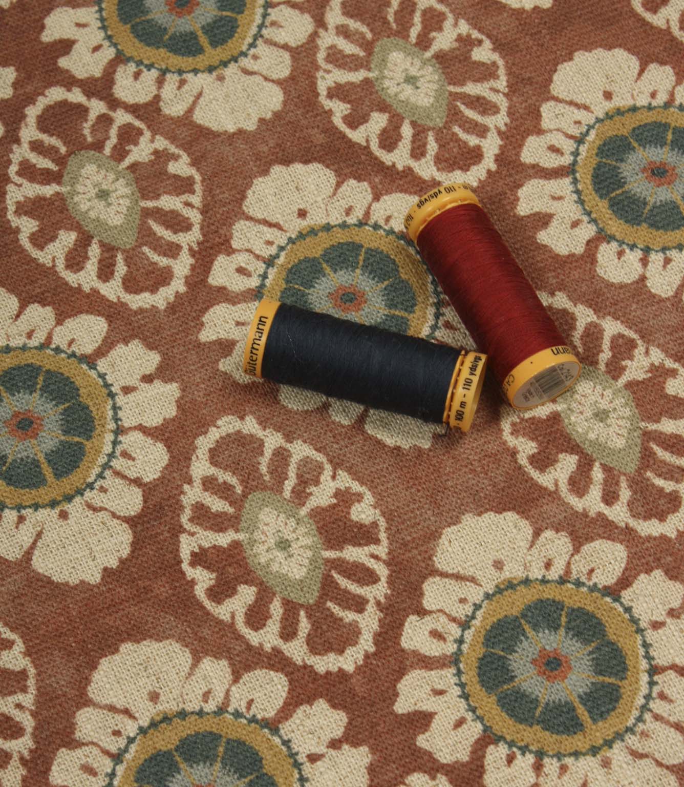 Terracotta floral print fabric styled with coordinating sewing threads to showcase rich warm tones and woven texture.
