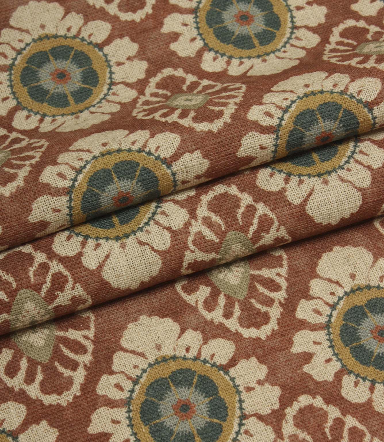 Folded terracotta red fabric with repeating floral medallion design, suitable for curtains, blinds and upholstery projects.