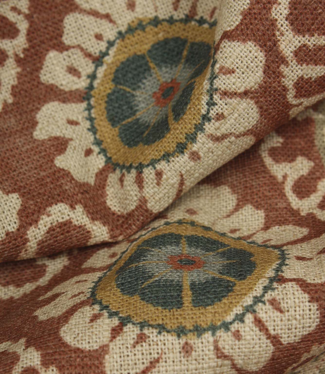 Close-up detail of terracotta and blue floral medallion fabric on a rustic woven base cloth.