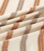 Close-up of Meschutt Coralee fabric draped in soft folds, highlighting raised terracotta and taupe embroidered stripes with zigzag edges and fine central stitching on ivory fabric.