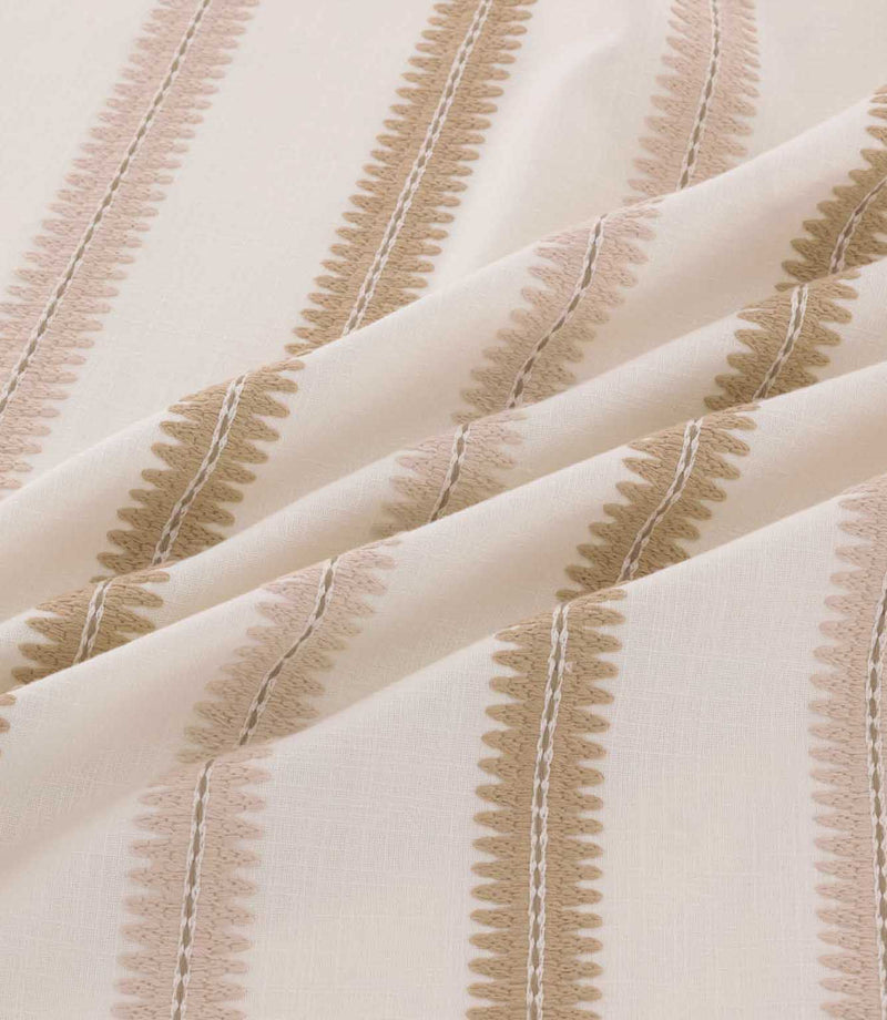 Close-up of Meschutt Shell fabric arranged in soft folds, highlighting textured blush pink and beige embroidered stripes with decorative zigzag edges on an ivory background.