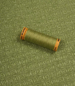 Nessa woven fabric with matching green thread spool, demonstrating the fabric's pattern and colour coordination.