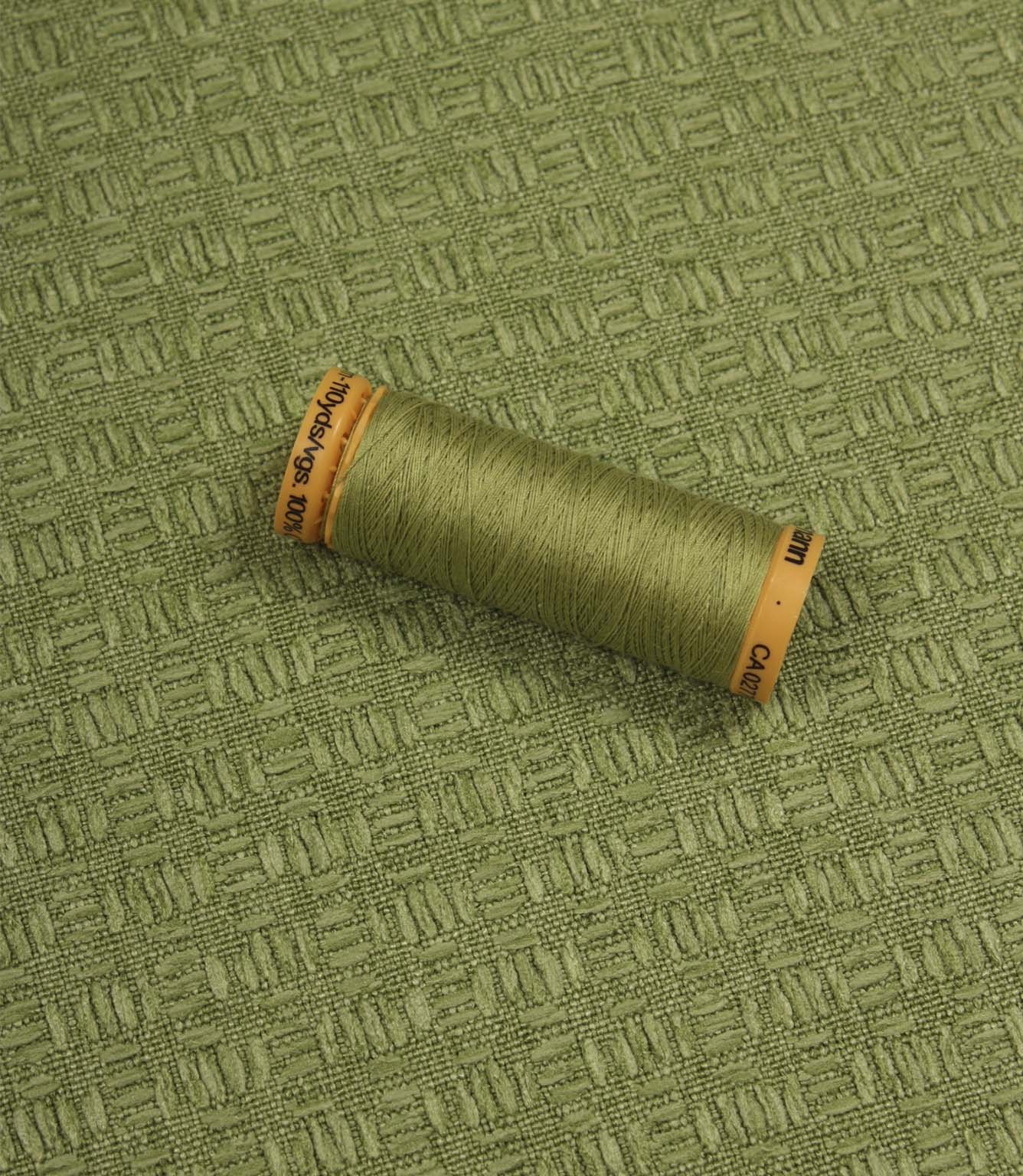 Nessa woven fabric with matching green thread spool, demonstrating the fabric's pattern and colour coordination.