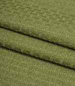 Folded Nessa woven fabric in green, showing the structured geometric texture and quality finish.