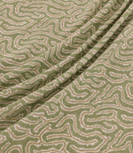 Noyack Kelp fabric arranged in soft, flowing folds, showcasing its muted olive green background and distinctive abstract pattern of winding cream and beige lines, with finely textured edges and a repeating organic design.