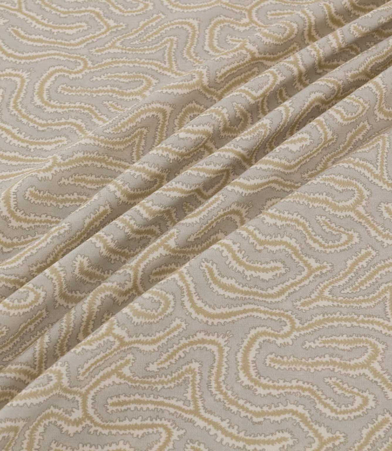 Noyack Quaker fabric arranged in soft, flowing folds, showcasing its light taupe background and distinctive abstract pattern of winding cream and beige lines, with finely textured edges and an intricate repeating design.