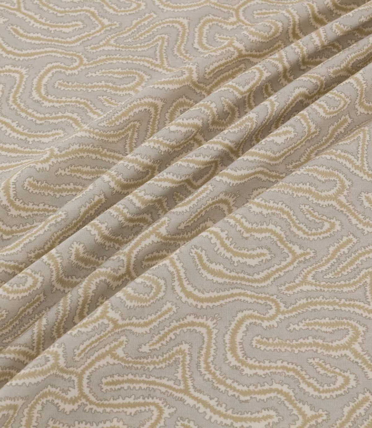 Noyack Quaker fabric arranged in soft, flowing folds, showcasing its light taupe background and distinctive abstract pattern of winding cream and beige lines, with finely textured edges and an intricate repeating design.