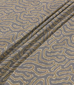 Noyack Rockport fabric arranged in soft, flowing folds, showcasing its muted slate grey background and distinctive abstract pattern of winding taupe and cream lines. The close-up highlights the intricate feathered edges, woven texture and natural drape of the fabric.