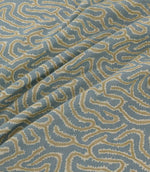 Noyack Saltwater fabric arranged in soft, flowing folds, showcasing its muted duck egg blue background and distinctive abstract pattern of winding cream and warm beige lines, with textured edges and a repeating organic design.