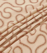 Close-up of Orient Coralee fabric draped in soft folds, showing terracotta embroidered wavy lines on a cream woven base and detailed stitching.