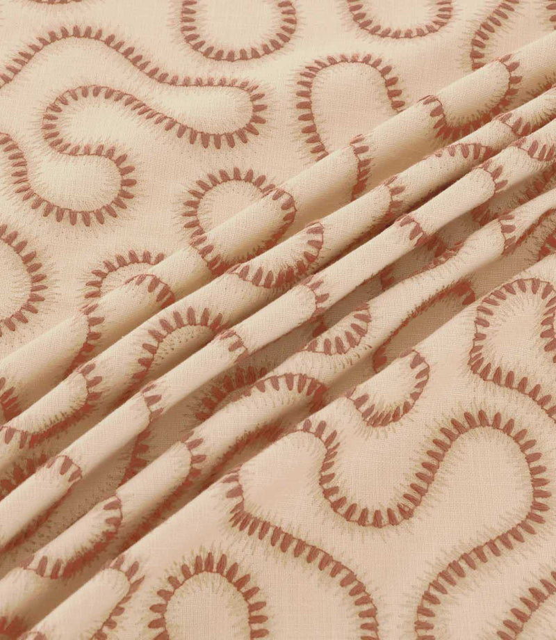 Close-up of Orient Coralee fabric draped in soft folds, showing terracotta embroidered wavy lines on a cream woven base and detailed stitching.