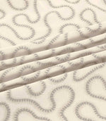 Orient Gull fabric gathered into gentle folds, highlighting its soft grey embroidered abstract pattern and textured ivory woven background.