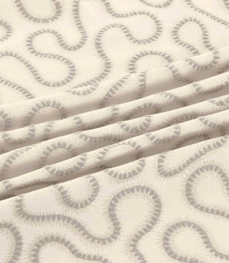 Orient Gull fabric gathered into gentle folds, highlighting its soft grey embroidered abstract pattern and textured ivory woven background.