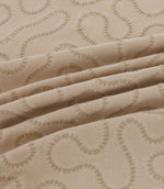 Close-up of draped Orient Quaker fabric showing raised tonal beige embroidery in a flowing wavy pattern on a natural woven base.