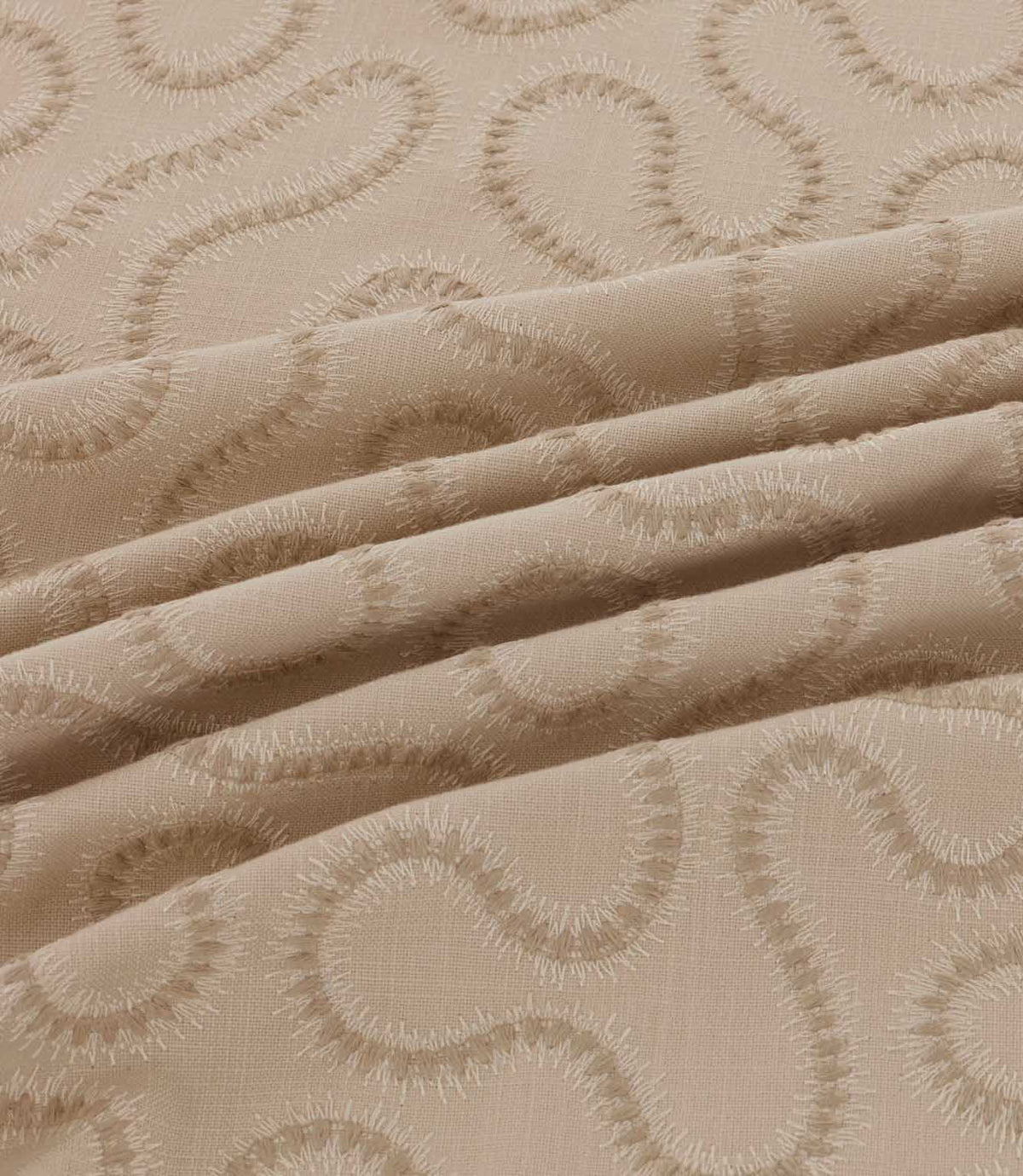 Close-up of draped Orient Quaker fabric showing raised tonal beige embroidery in a flowing wavy pattern on a natural woven base.