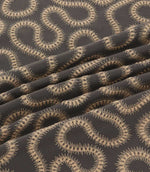 Orient Rockport embroidered fabric arranged in soft folds, showing detailed beige wavy stitching against a contrasting charcoal woven background.