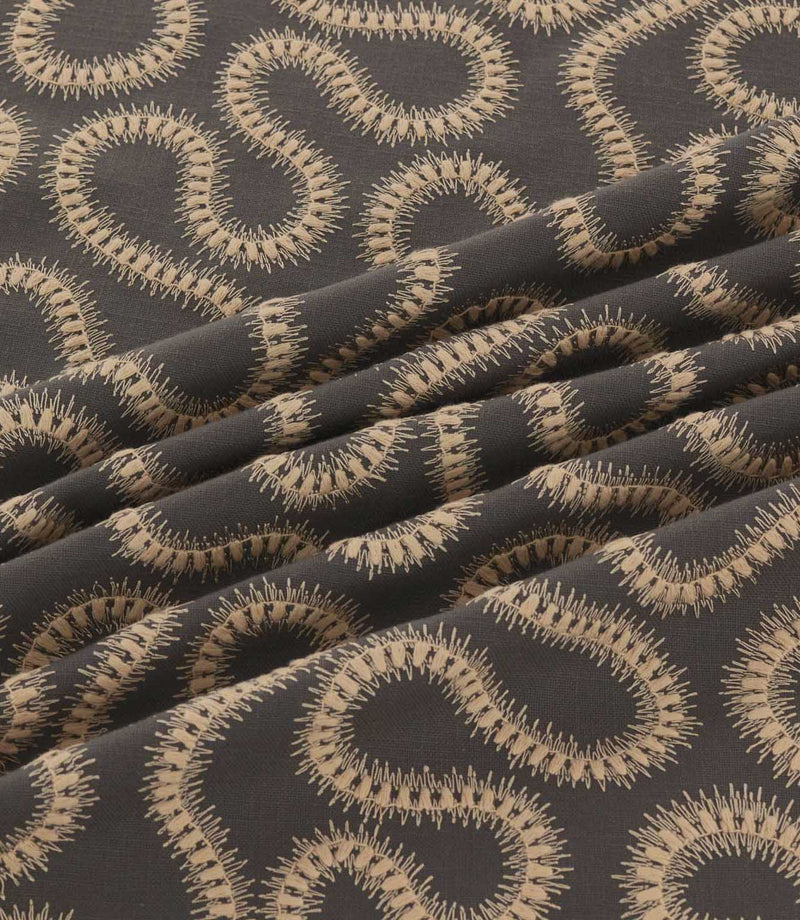 Orient Rockport embroidered fabric arranged in soft folds, showing detailed beige wavy stitching against a contrasting charcoal woven background.