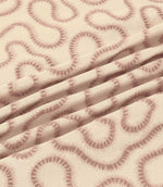 Orient Shell fabric gathered into soft folds, highlighting dusty pink embroidered flowing lines and the subtle texture of its ivory woven base.