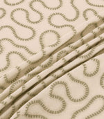 Close-up of Orient Willow fabric draped in gentle folds, showing olive green embroidered wavy lines on a natural cream woven background.