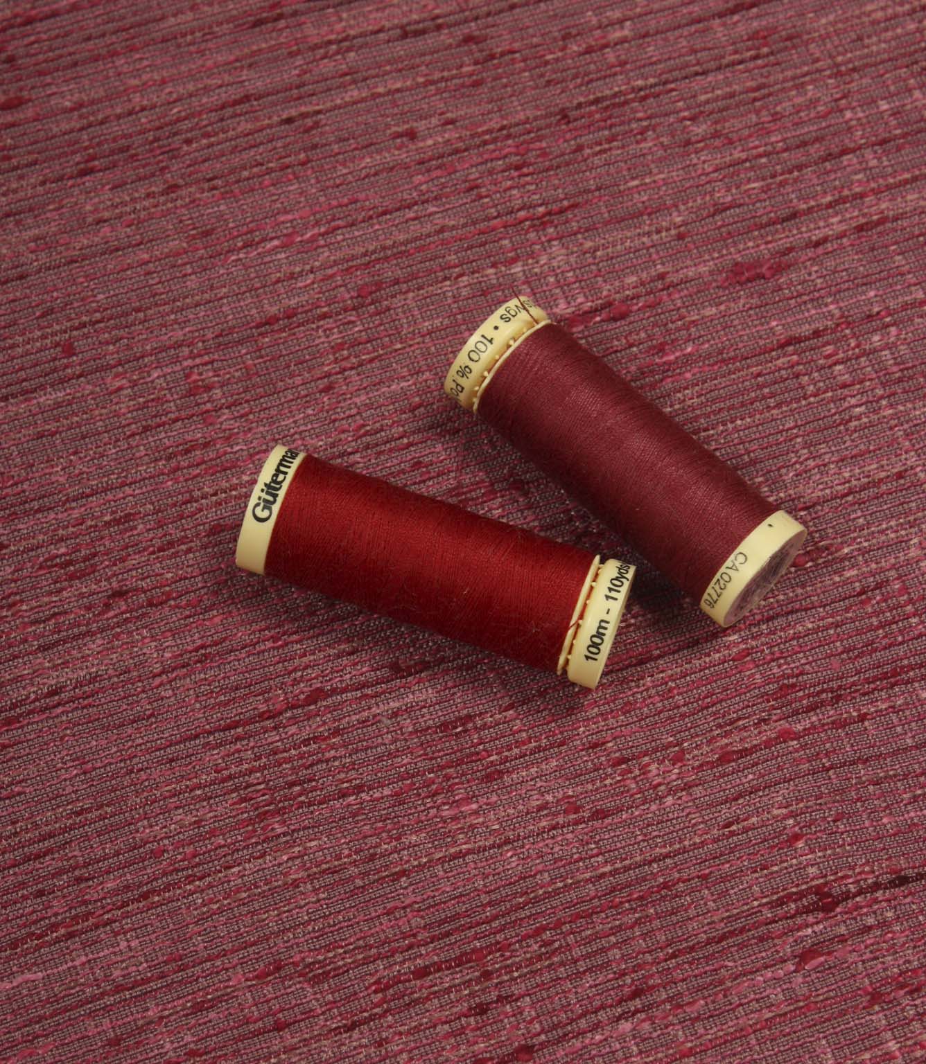 Otaru woven plain fabric with matching red thread spools, showing the fabric texture and colour coordination.