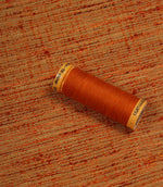 Otaru woven plain fabric in sunset orange with coordinating thread spool, illustrating the fabric's texture, colour depth and woven character.