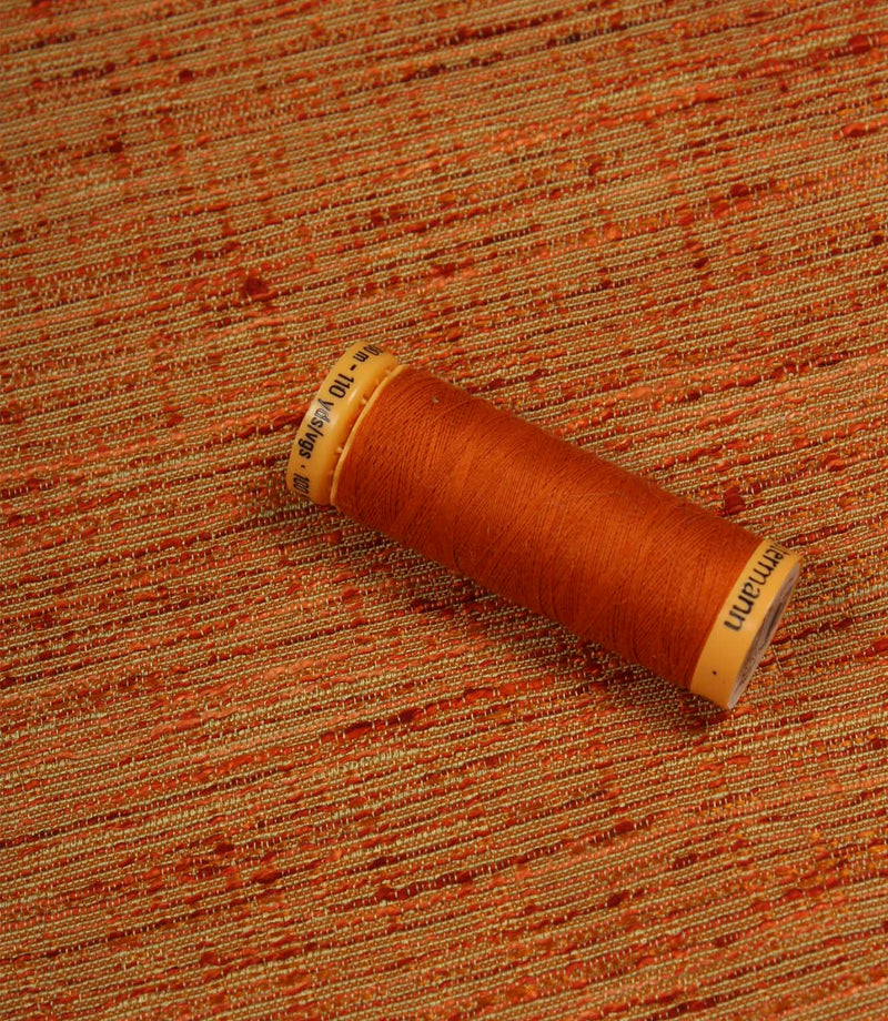 Otaru woven plain fabric in sunset orange with coordinating thread spool, illustrating the fabric's texture, colour depth and woven character.