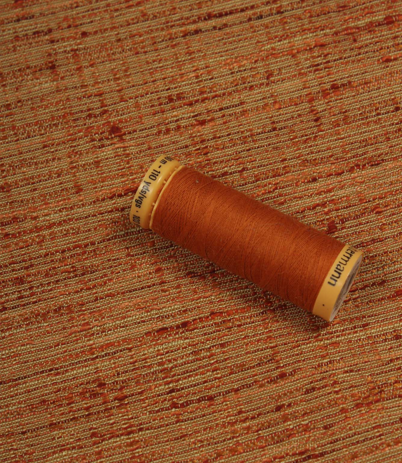 Otaru woven plain fabric in sunset orange with coordinating thread spool, illustrating the fabric's texture, colour depth and woven character.