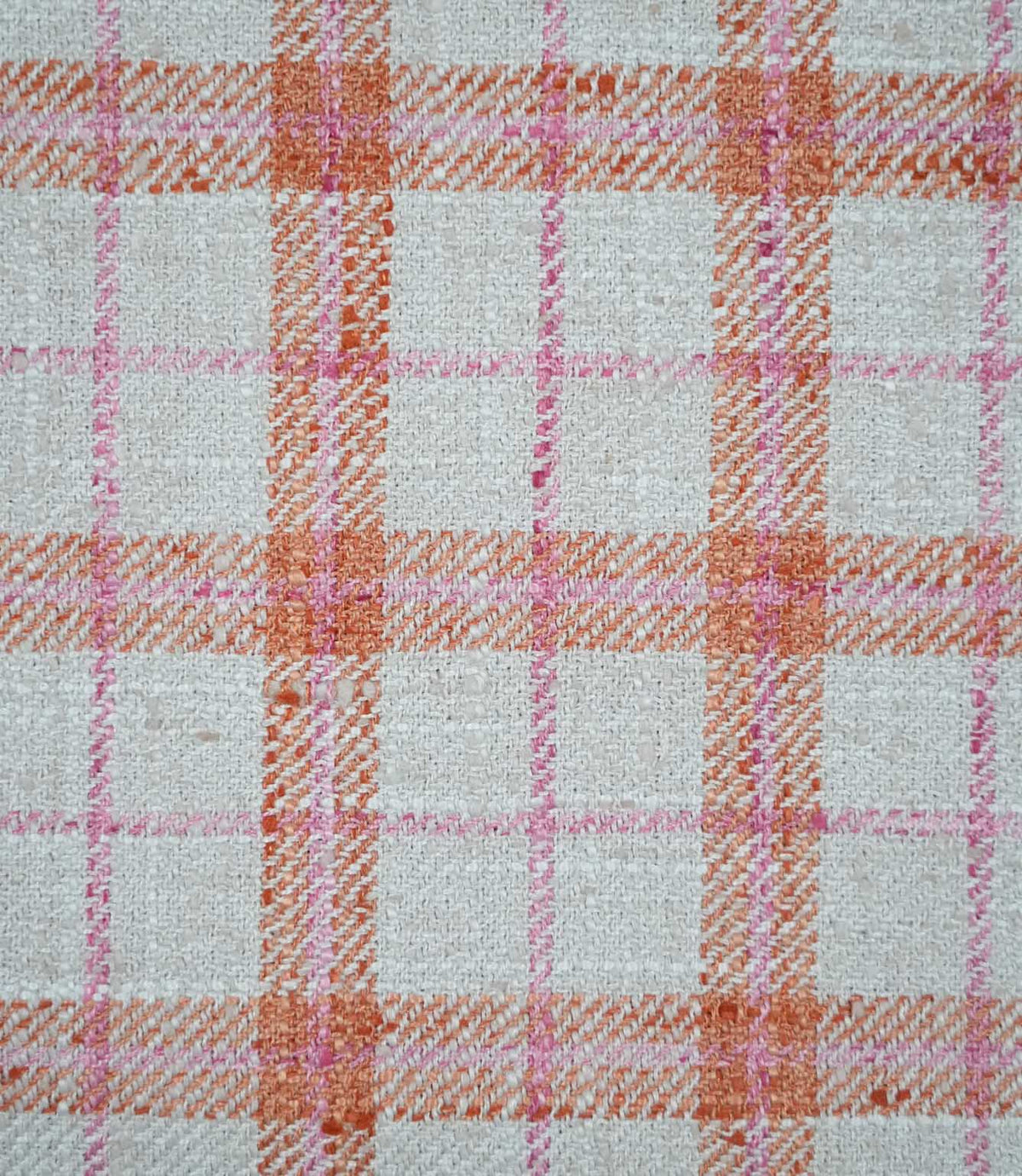 Close-up of Painswick Check Russett fabric showing a detailed woven check design with textured russet orange bands, delicate pink lines and a natural cream base, highlighting the interwoven yarns and subtle diagonal detailing.