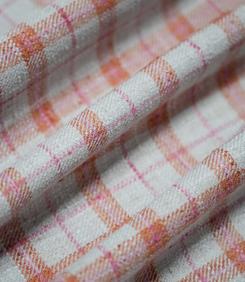 Painswick Check Russett fabric arranged in soft, overlapping folds, highlighting its textured weave and traditional checked pattern of warm russet orange bands and fine pink lines against a natural cream background.