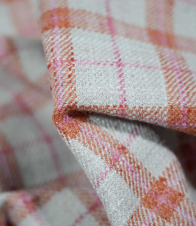 Macro photograph of Painswick Check Russett fabric showing its textured woven surface, with interlacing cream, russet orange and pink yarns forming a classic check pattern with subtle diagonal weave details.