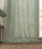 Full-length Perrie Leaf sheer curtain panel in forest green and soft white, softly filtering daylight beside a glazed door in a natural living space.