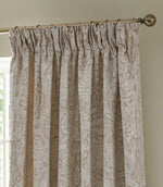 Morris & Co Pimpernel cream and beige jacquard pencil pleat curtain hanging from a metal curtain pole, showing the detailed woven botanical pattern and gathered heading.