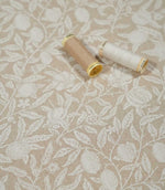 Pomegranate Linen Look William Morris fabric in warm beige and cream with thread reels, showing the detailed botanical pattern and woven texture