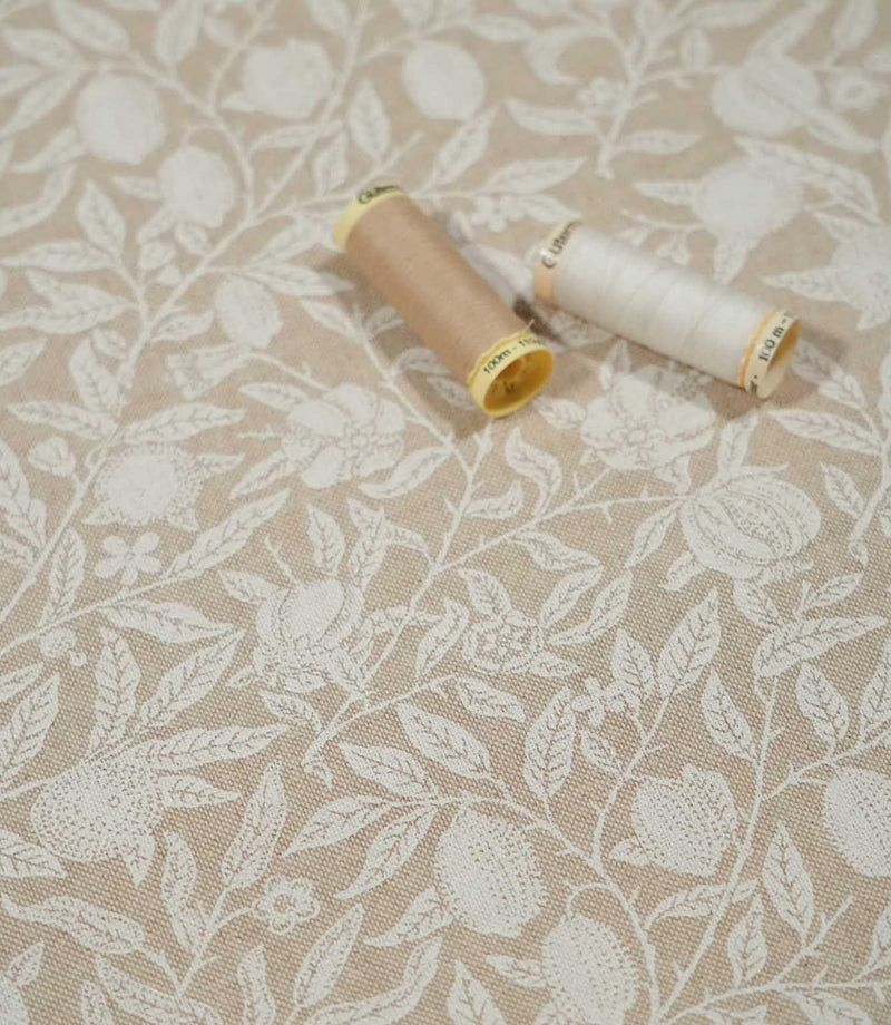 Pomegranate Linen Look William Morris fabric in warm beige and cream with thread reels, showing the detailed botanical pattern and woven texture