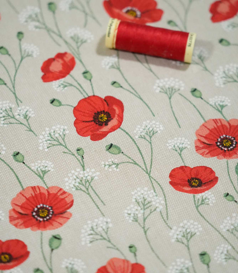 Poppy Trail Red floral fabric photographed with a red sewing thread spool for scale, highlighting the detailed poppy print, fine green stems and natural woven texture.