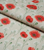 Poppy Trail Red fabric folded over itself, showing the repeating red and coral poppy design, delicate white wildflowers and textured beige woven surface.