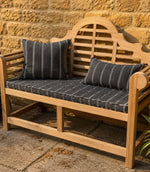 Wooden bench with striped outdoor fabric cushions against a stone wall