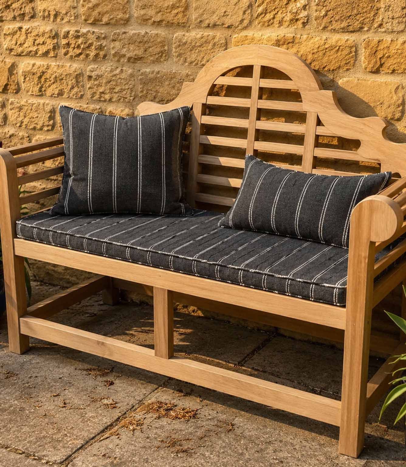 Wooden bench with striped outdoor fabric cushions against a stone wall