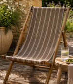 Wooden deck chair with striped brown outdoor fabric on a wooden deck, in a garden setting