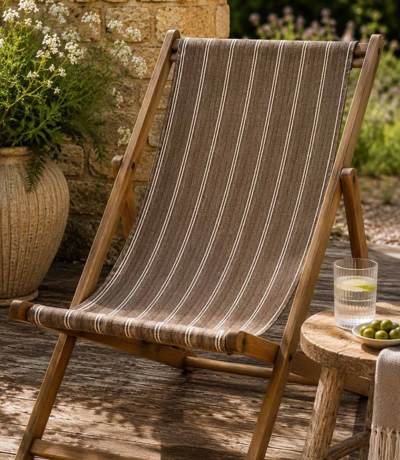 Wooden deck chair with striped brown outdoor fabric on a wooden deck, in a garden setting